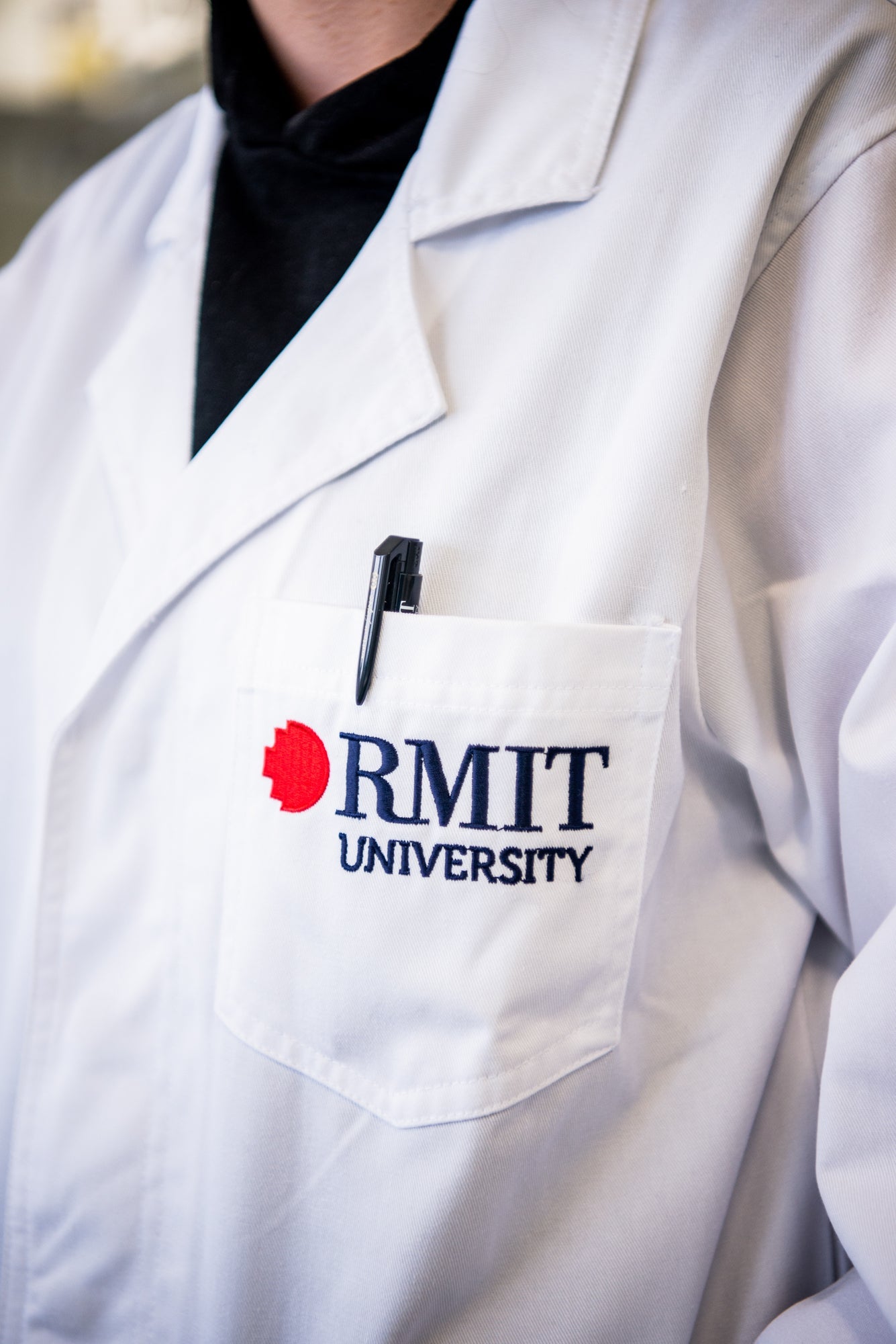 Close-up of a white RMIT University lab coat with a black pen neatly placed in the chest pocket, highlighting the embroidered logo.